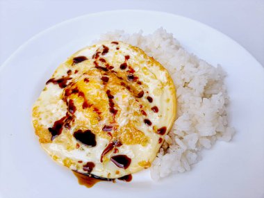 Beyaz arka planda izole edilmiş beyaz bir tabakta beyaz pirinç ve soya sosuyla servis edilen kızarmış yumurta ya da güneşli tarafı. Metin için boşluk