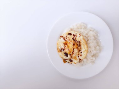 Beyaz arka planda izole edilmiş beyaz bir tabakta beyaz pirinç ve soya sosuyla servis edilen kızarmış yumurta ya da güneşli tarafı. Metin için boşluk