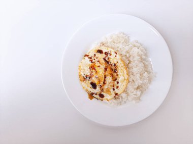 Beyaz arka planda izole edilmiş beyaz bir tabakta beyaz pirinç ve soya sosuyla servis edilen kızarmış yumurta ya da güneşli tarafı. Metin için boşluk