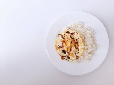 Beyaz arka planda izole edilmiş beyaz bir tabakta beyaz pirinç ve soya sosuyla servis edilen kızarmış yumurta ya da güneşli tarafı. Metin için boşluk