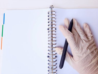 Beyaz lateks eldivenli bir el siyah bir kalem tutar, kitaba yaz. Beyaz arkaplanda, kenar görünümde izole edilmiş