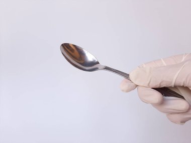 Beyaz lateks eldivenli bir el metal kaşık tutar. Beyaz bir arkaplanda izole edilmiş