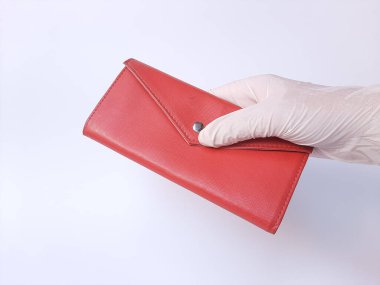 Beyaz lateks eldivenli bir el kırmızı bir çanta tutar. Beyaz bir arka planda izole edilmiş. Metin için boşluk