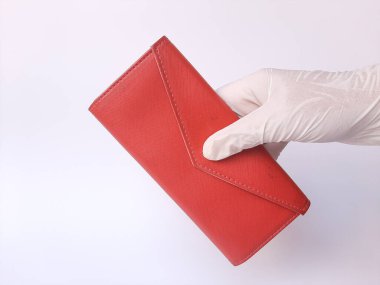 Beyaz lateks eldivenli bir el kırmızı bir çanta tutar. Beyaz bir arka planda izole edilmiş. Metin için boşluk