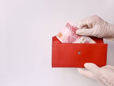 İki el beyaz lateks eldiven içinde kırmızı bir çanta içinde 100.000 IDR, Endonezya banknotları. Beyaz arka planda izole edilmiş. Yan görünüm.