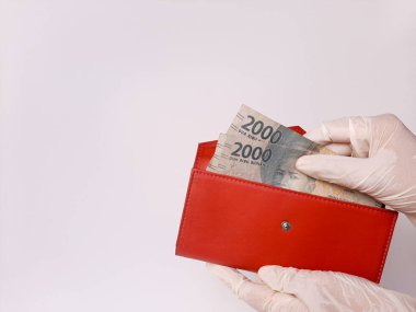 Beyaz lateks eldivenli iki el biraz para tutuyor. 2000 IDR, Endonezya banknotları. Beyaz arka planda izole edilmiş. Yeni normal zamanda nakit ödeme yöntemi