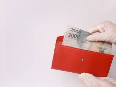 Beyaz lateks eldivenli iki el biraz para tutuyor. 2000 IDR, Endonezya banknotları. Beyaz arka planda izole edilmiş. Yeni normal zamanda nakit ödeme yöntemi