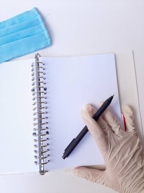 Beyaz lateks eldivenli, siyah kalemli, boş beyaz ciltli bir el. Beyaz bir arka planda izole edilmiş. Üst görünüm veya düz görünüm veya genel görünüm