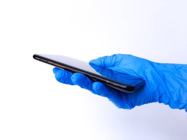 Siyah cep telefonu tutan beyaz lateks eldivenli bir el. Beyaz bir arkaplanda izole edilmiş