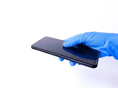 Siyah cep telefonu tutan beyaz lateks eldivenli bir el. Beyaz bir arkaplanda izole edilmiş