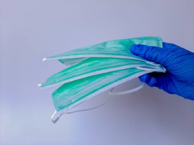 Mavi lateks eldivenli bir el, tıbbi ya da cerrahi maske tutuyor. Beyaz arkaplanda izole edilmiş