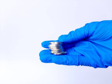 Beyaz lateks eldivenli bir elin içinde gümüş paralar var. Beyaz arka planda izole edilmiş. Yan görünüm.