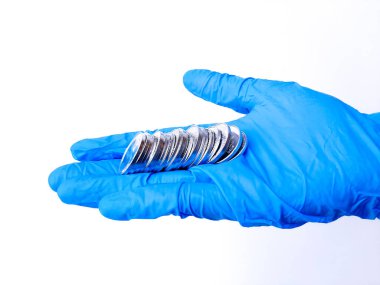 Beyaz lateks eldivenli bir elin içinde gümüş paralar var. Beyaz arka planda izole edilmiş. Yan görünüm.