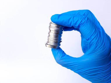 Beyaz lateks eldivenli bir elin içinde gümüş paralar var. Beyaz arka planda izole edilmiş. Yan görünüm.