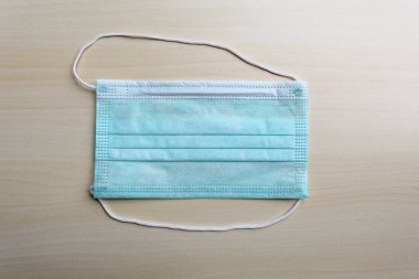Bir parça tıbbi ya da cerrahi maske, sarı ahşap yüzeyin üstünde.