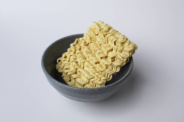 Pişmeden önce kare hazır erişte, gri kasenin içinde, beyaz arka planda izole edilmiş.