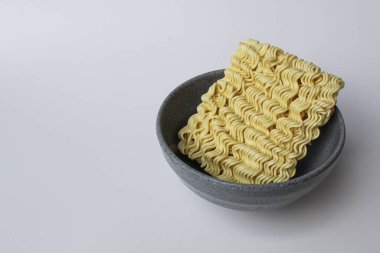 Pişmeden önce kare hazır erişte, gri kasenin içinde, beyaz arka planda izole edilmiş.