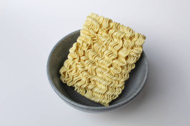 Pişmeden önce kare hazır erişte, gri kasenin içinde, beyaz arka planda izole edilmiş.