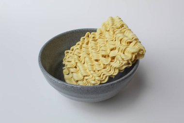 Pişmeden önce kare hazır erişte, gri kasenin içinde, beyaz arka planda izole edilmiş.