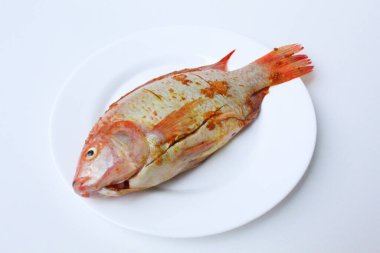 Red Nile Tilapia, Red Tilapia, veya Oreochromis niloticus. Ezilmiş zerdeçal ile tatlandırılmış taze balık. Beyaz arka planda izole edilmiş pembe kasenin içinde.