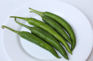Beyaz bir tabakta, beyaz arka planda izole edilmiş uzun yeşil biberler.