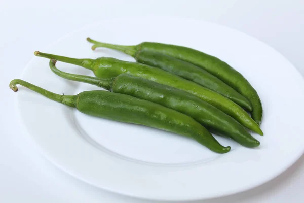 Long big green chillies, on a white plate, isolated on white background