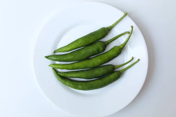Long big green chillies, on a white plate, isolated on white background. Flat lay or top view