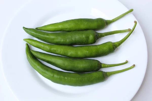 Long big green chillies, on a white plate, isolated on white background