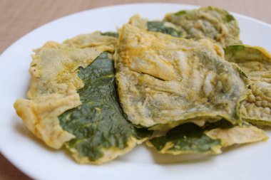 Kızarmış yeşil amaranth yaprakları veya ıspanak yaprakları, beyaz bir tabakta un hamuru ile kaplıdır..