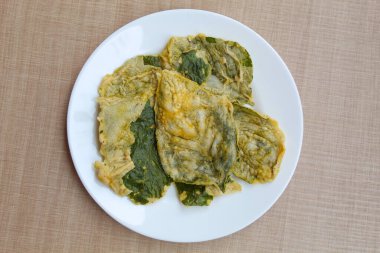 Kızarmış yeşil amaranth yaprakları ya da ıspanak yaprakları, beyaz bir tabakta un hamuru ile kaplıdır. Düz ya da üst görünüm.