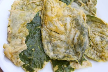 Kızarmış yeşil amaranth yaprakları ya da ıspanak yaprakları, beyaz bir tabakta un hamuru ile kaplıdır. Düz ya da üst görünüm.