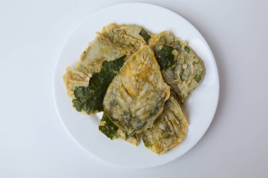 Kızarmış yeşil amaranth yaprakları ya da ıspanak yaprakları, beyaz bir tabakta un hamuru ile kaplıdır. Beyaz arka planda izole edilmiş. Düz ya da üst görünüm.