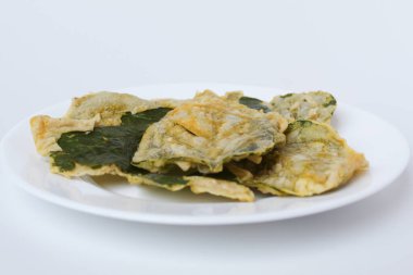 Kızarmış yeşil amaranth yaprakları ya da ıspanak yaprakları, beyaz bir tabakta un hamuru ile kaplıdır. Beyaz arkaplanda izole.