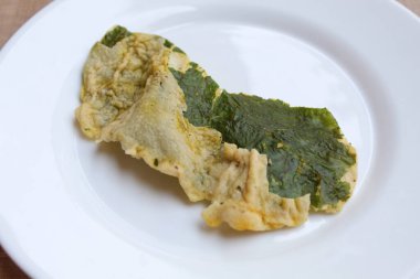 Kızarmış yeşil amaranth yaprakları ya da ıspanak yaprakları, beyaz bir tabakta un hamuru ile kaplıdır. Beyaz arkaplanda izole.