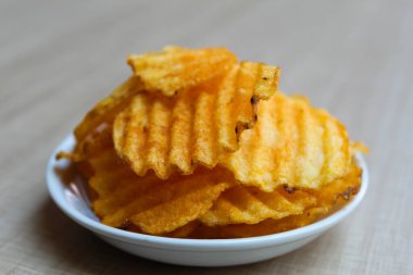 Dalgalı patates cipsi, kırmızı pudra çeşnili, küçük bir tabakta. Ahşap arkaplan.