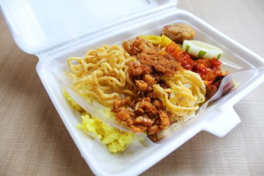 Nasi kuning, Endonezya 'dan geleneksel bir yemektir. Sarı pirinç, erişte, tavuk ipi, omlet ve çeşitli mezelerden oluşur. Satılık köpük kutusuna yerleştirilmiş..