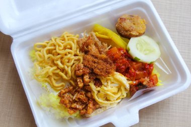 Nasi kuning, Endonezya 'dan geleneksel bir yemektir. Sarı pirinç, erişte, tavuk ipi, omlet ve çeşitli mezelerden oluşur. Satılık köpük kutusuna yerleştirilmiş..