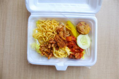 Nasi kuning, Endonezya 'dan geleneksel bir yemektir. Sarı pirinç, erişte, tavuk ipi, omlet ve çeşitli mezelerden oluşur. Satılık köpük kutusuna yerleştirilmiş..