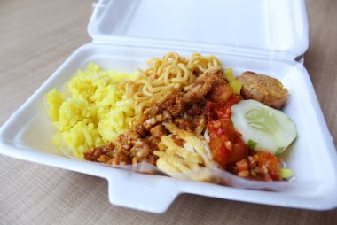 Nasi kuning, Endonezya 'dan geleneksel bir yemektir. Sarı pirinç, erişte, tavuk ipi, omlet ve çeşitli mezelerden oluşur. Satılık köpük kutusuna yerleştirilmiş..