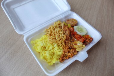 Nasi kuning, Endonezya 'dan geleneksel bir yemektir. Sarı pirinç, erişte, tavuk ipi, omlet ve çeşitli mezelerden oluşur. Satılık köpük kutusuna yerleştirilmiş..