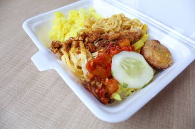 Nasi kuning, Endonezya 'dan geleneksel bir yemektir. Sarı pirinç, erişte, tavuk ipi, omlet ve çeşitli mezelerden oluşur. Satılık köpük kutusuna yerleştirilmiş..