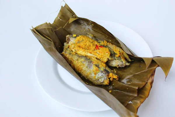 Pepes ikan, or steamed fish with herbs then wrapped in banana leaf. Indonesia traditional food. On a white plate.