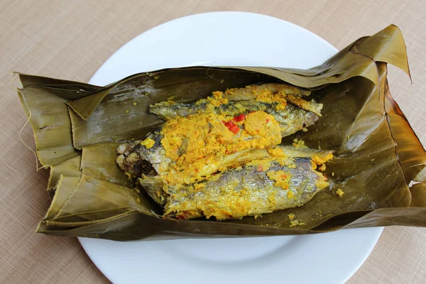 Pepes ikan, or steamed fish with herbs then wrapped in banana leaf. Indonesia traditional food. Wooden background.