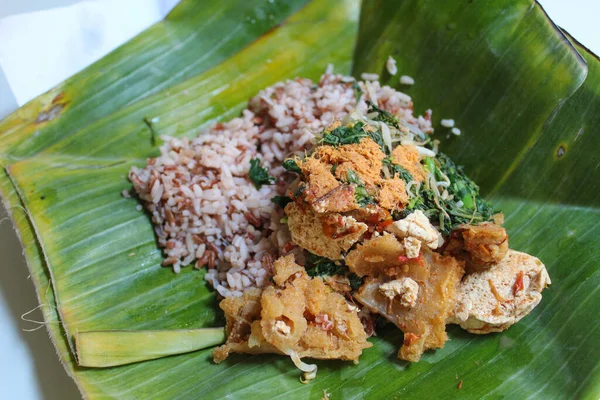 Red rice with steamed vegetables, tofu and grated coconut. Served on banana leaf.
