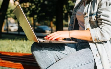 Serbest çalışma, uzaktan çalışma, ofis açık hava konsepti. Parkta, yan görüntüde dizüstü bilgisayarda yazı yazan kadınların yakın çekimleri. Kırmızı manikürlü kadın ellerine odaklan..