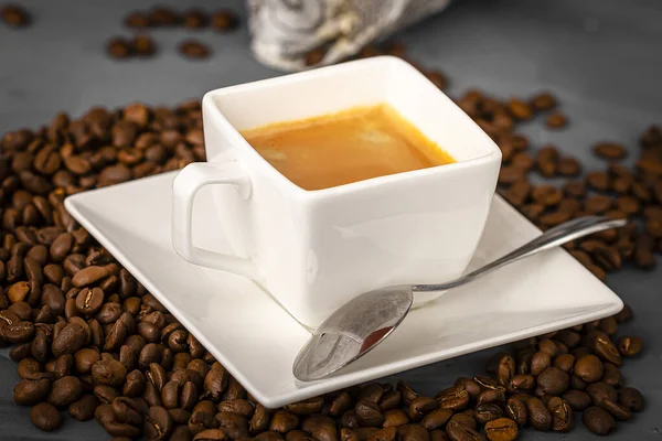散在するコーヒー豆の背景にエスプレッソコーヒーの白いカップとソーサー。コーヒーを作る. — ストック写真
