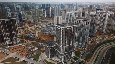 Modern çok katlı binaların yapımı. Yeni bir şehir bloğu inşaatı. İnşaat halindeki binalar ve kule vinçleri. Bulutlu havada hava fotoğrafçılığı.