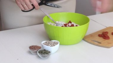 Yeşil karabuğdaydan ekmek yapmak. Bir kadın yeşil karabuğday hamuruna kurutulmuş kayısı ekler. Masanın yanında keten, ayçiçeği ve balkabağı tohumları var..