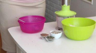 Yeşil karabuğdaydan ekmek yapmak. Bir kadın mikserde yeşil karabuğday öğütüyor. Yakındaki kaplarda keten, balkabağı ve ayçekirdeği var..