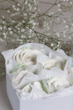 Hediye kutusunda ev yapımı marşmelov. Zephyr gülleri. Kalp şeklinde bir kutu. Fiyonka bağlanmış bir kurdeleyle bağlanmış. Şekerleme gülleri. Kalp şeklinde bir kutu. Yakınlarda bir buket çigila var..